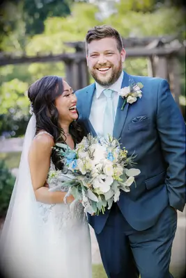 bride and groom laughing while bride holds light blue and white wedding bouquet 