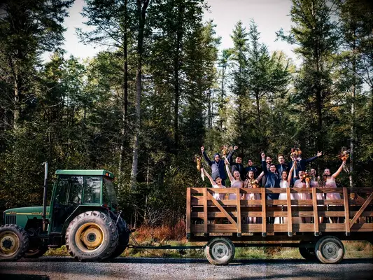 Bride and groom with bridesmaids and groomsmen on hay bale tractor at rustic barn wedding