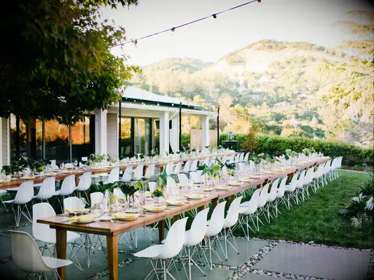 outdoor wedding reception with long bare wood banquet tables and white molded chairs