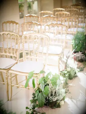 rows of gold opera chairs at wedding ceremony with greenery aisle markers