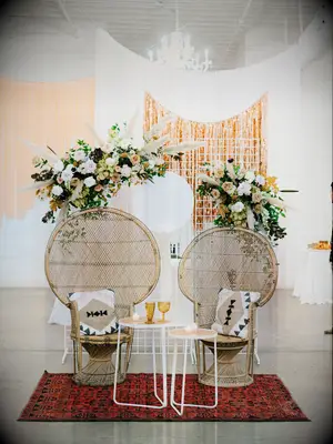 two peacock chairs with end tables, kilim rug and hanging pampas grass floral installation