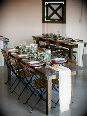 rustic modern indoor wedding reception bare wooden table with white gauze runner and wooden slotted chairs