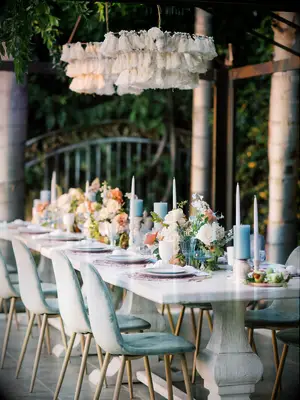 long banquet table at outdoor wedding reception with fringe chandeliers and light blue velvet chairs