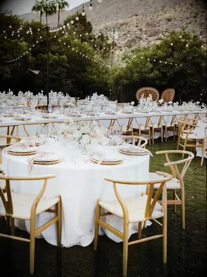 modern outdoor wedding reception with round banquet tables decorated in white linens and light wood wishbone chairs