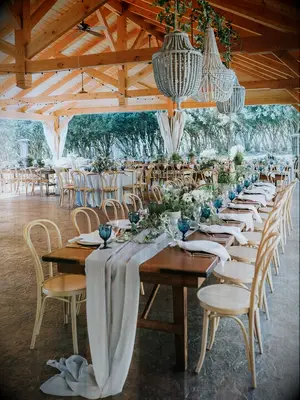 long wedding banquet table with light wooden bentwood cafe chairs underneath beaded boho chandelier