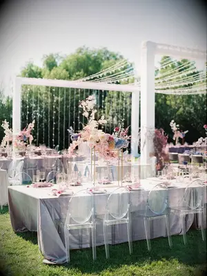 modern outdoor wedding reception with long banquet tables in lilac iridescent table linens and round ghost chairs 