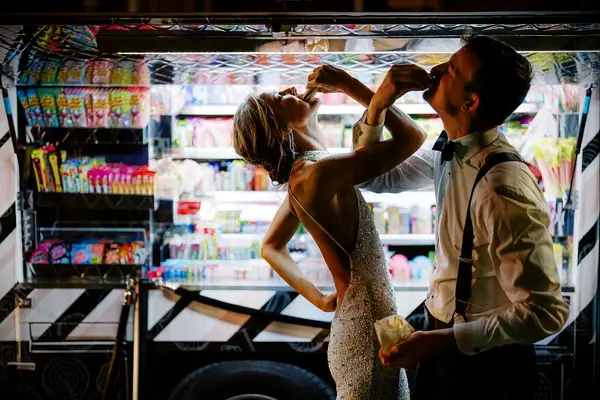 Bride and groom enjoying late night snack after wedding in gas station