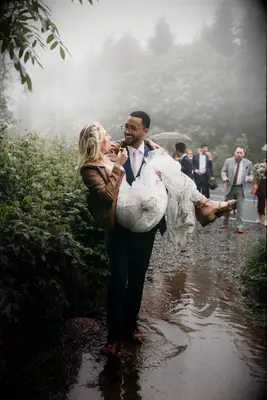 Groom carrying bride through the rain after ceremony