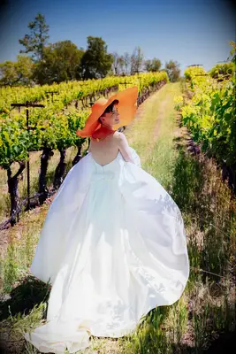 Bride in Strapless Wedding Dress and Oversized Orange Hat in Vineyard