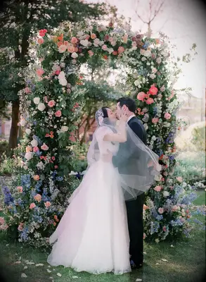 Couple kissing in front of multicolored floral arch at ceremony