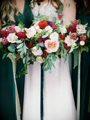 Bridesmaids in green dresses holding red dahlia bouquets