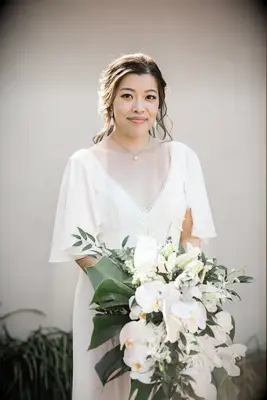 bride holding modern tropical wedding bouquet with banana leaves, white phalaenopsis orchids and white anthuriums 