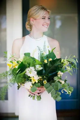bride holding oversized summer wedding bouquet with monstera leaves, plumosa ferns, yellow alstroemeria and orchids