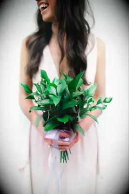 bridesmaid wearing a sleeveless blush dress holds a bouquet of green ruscus tied with white ribbons