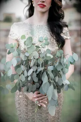bride wearing gold sequined dress holds loose wedding bouquet with branches of silver dollar eucalyptus