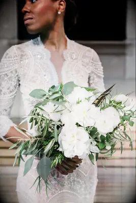 bride holding bouquet with white flowers, bay leaves, eucalyptus and brown pheasant feathers