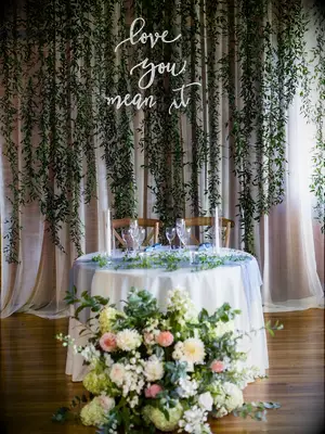 Curtain of hanging vines with neon sign behind sweetheart table at wedding reception