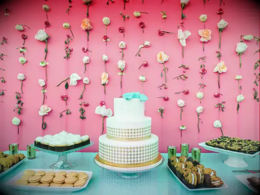 Individual flower stems taped on pink wall around wedding cake and dessert spread