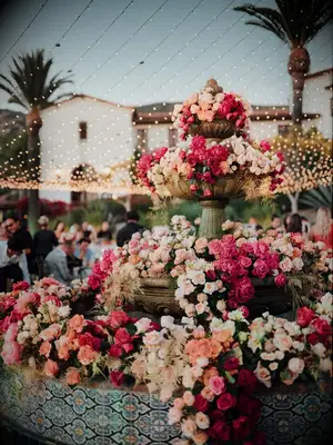 Tiered Fountain With Spilling Flower Arrangements in Pink and Blush Under String Lights