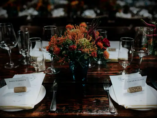 fall wedding centerpiece with yellow pincushion proteas and orange mums on bare wood table