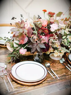 fall wedding centerpiece with burgundy leaves, pink flowers and greenery on bare wooden table