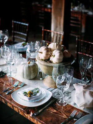 rustic fall wedding centerpiece with mini white pumpkins in stone urn vase on bare wooden table