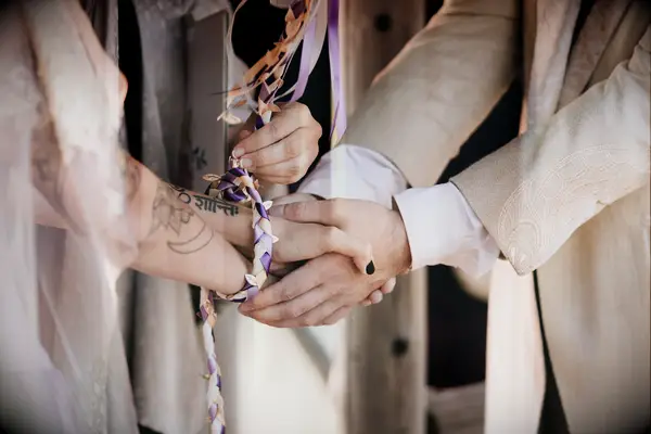 bride and groom holding hands during handfasting ceremony with purple braided rope