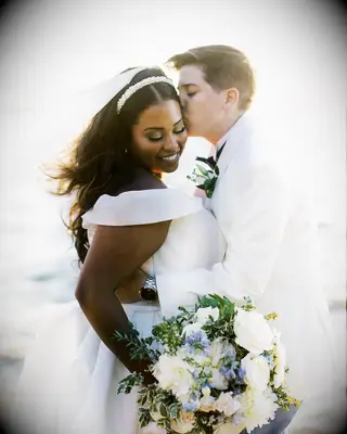 Couple in White, Suit and Wedding Dress, Kissing by the Ocean With Flowers