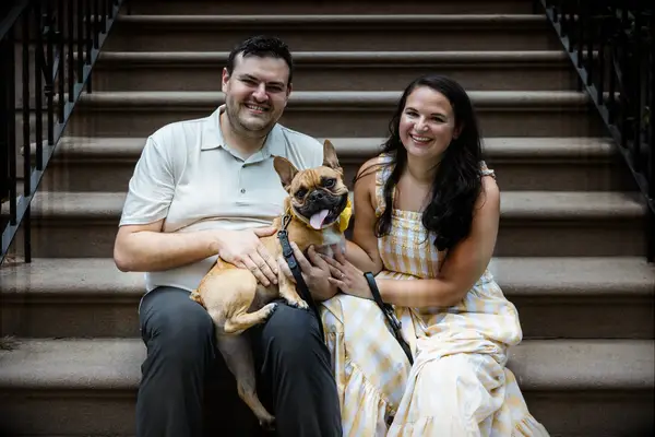 To-be-weds with their dog in their lap while sitting on a stoop.