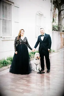 Bride and groom holding hands and posing with their dog.