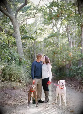 Happy couple kissing while holding their two dogs on a leash.