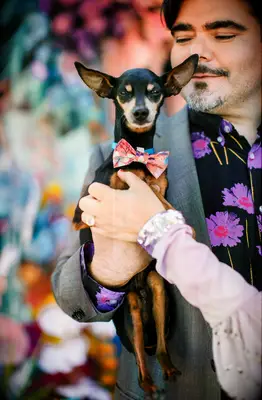 Groom holding dog wearing a colorful bow tie for a photo shoot.