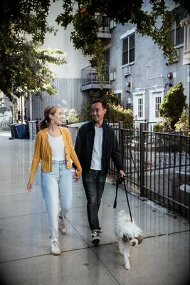 To-be-weds looking at each other while walking their dog. 