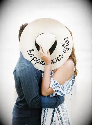 Couple kisses behind a large sun hat. 