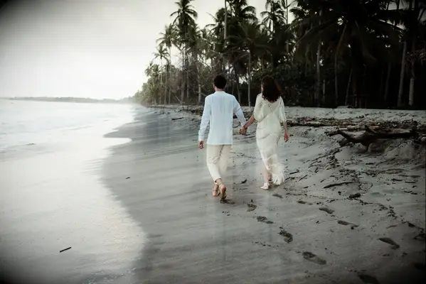 Couple holds hands and walks down the beach. 