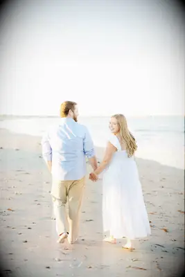 Couple walks down a beach while the bride looks back at the photographer. 