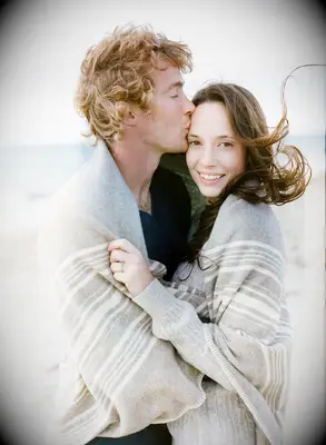 Couple wrapped in a blanket smile for the camera. 