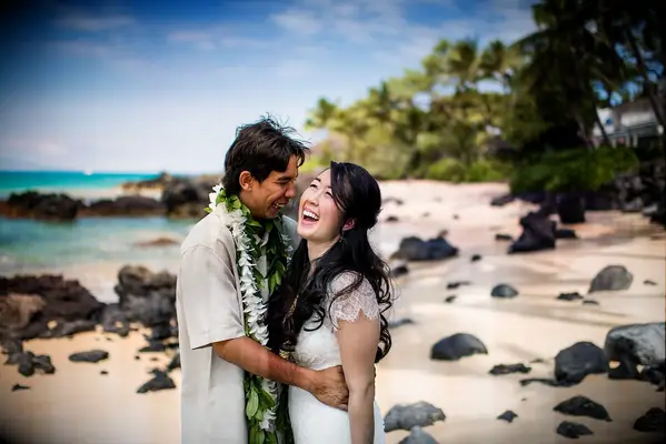 Couple laughs while embracing on a beach. 