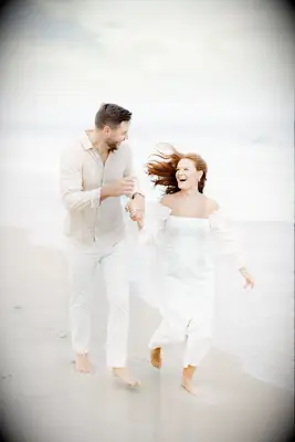 Couple holds hands while running down a beach. 