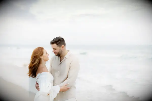 Couple embrace and look at each other lovingly on a beach. 