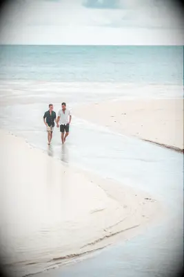 Couple walks through the water on a beach while holding hands. 