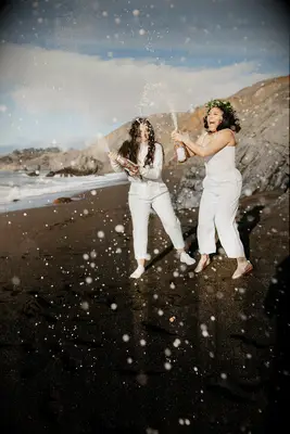 Couple pops champagne on the beach. 