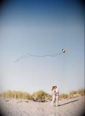Couple embraces on a beach while a kite flies above them. 