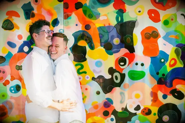 Grooms hugging in front of colorful mural