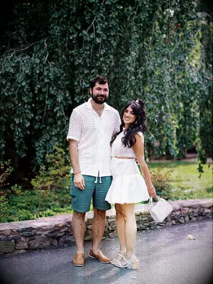 Couple posing and smiling together in front of tree wearing white 