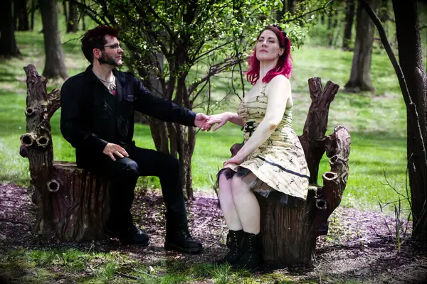 Couple poses for the camera while sitting on tree stumps. 