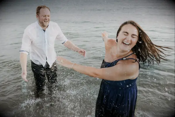 Couple splashes in the ocean during their engagement shoot. 