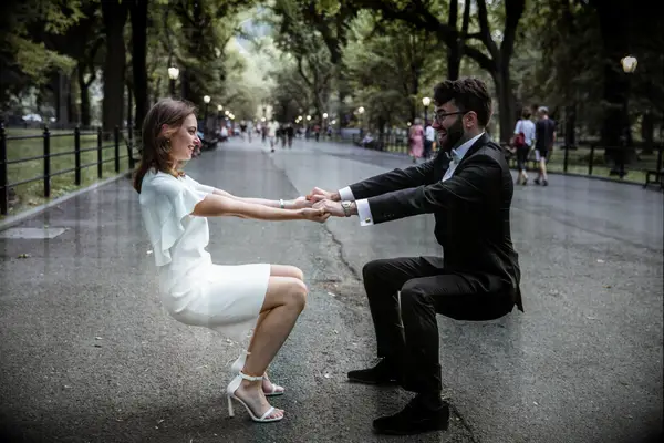 Couple holds hands and squats for a funny photograph in Central Park. 
