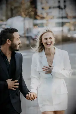 Couple holds hands and laughs while walking down the street. 