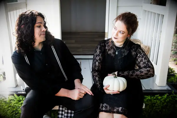 Couple wearing black clothing pose for the camera with a white pumpkin. 